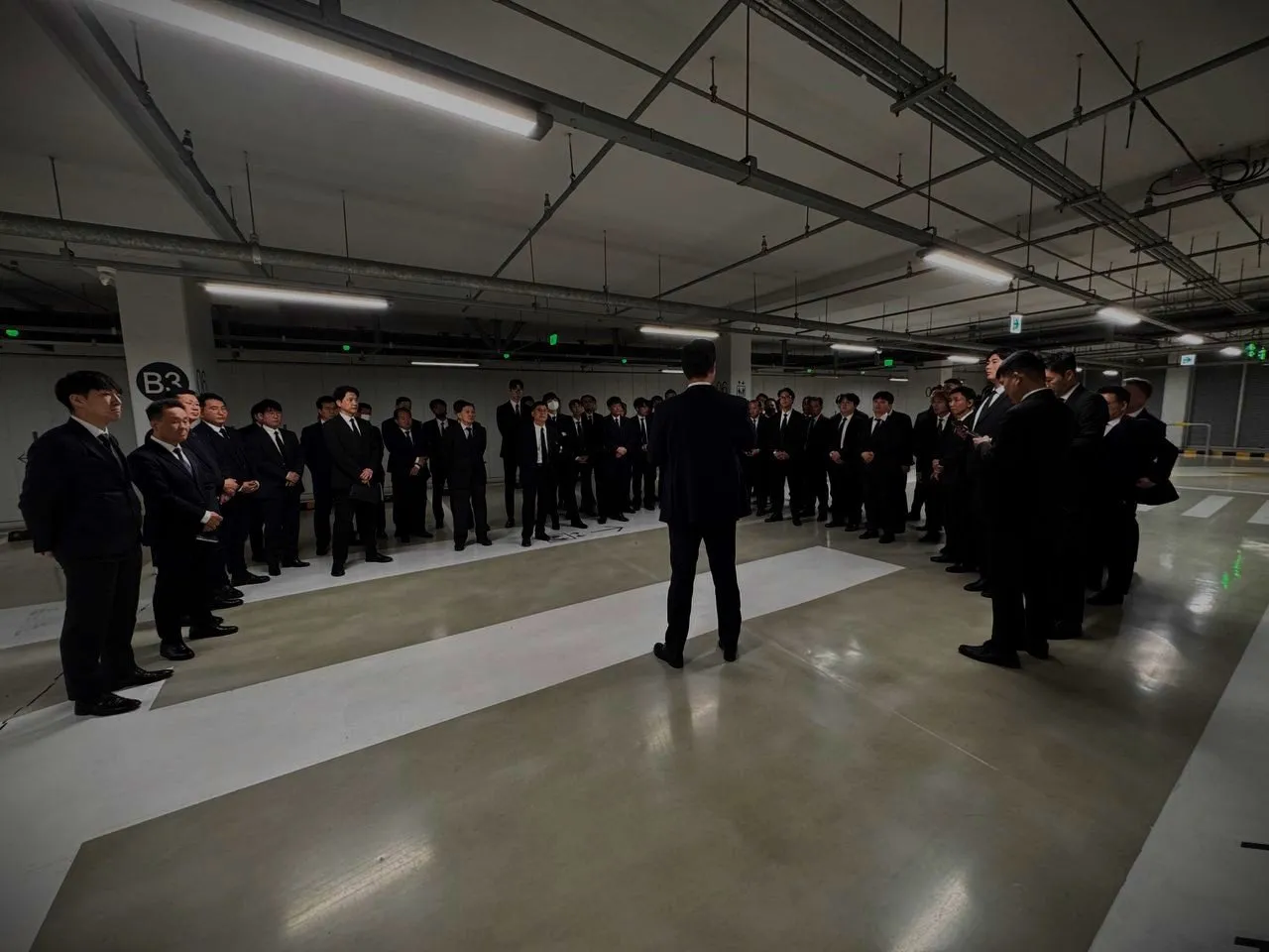Dozens of staff in suits being briefed in an underground car park before an event